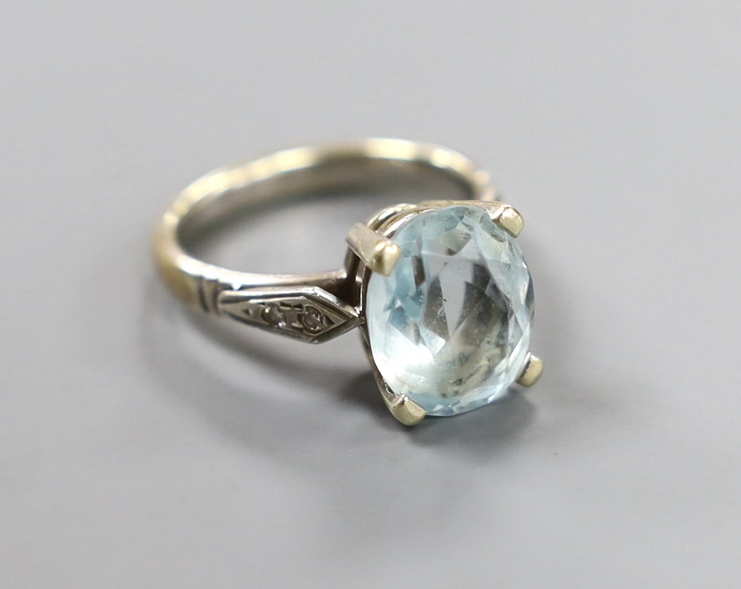 A modern yellow and white metal, oval cut aquamarine set dress ring, with diamond chip set shoulders, size N, gross weight 5.6 grams.